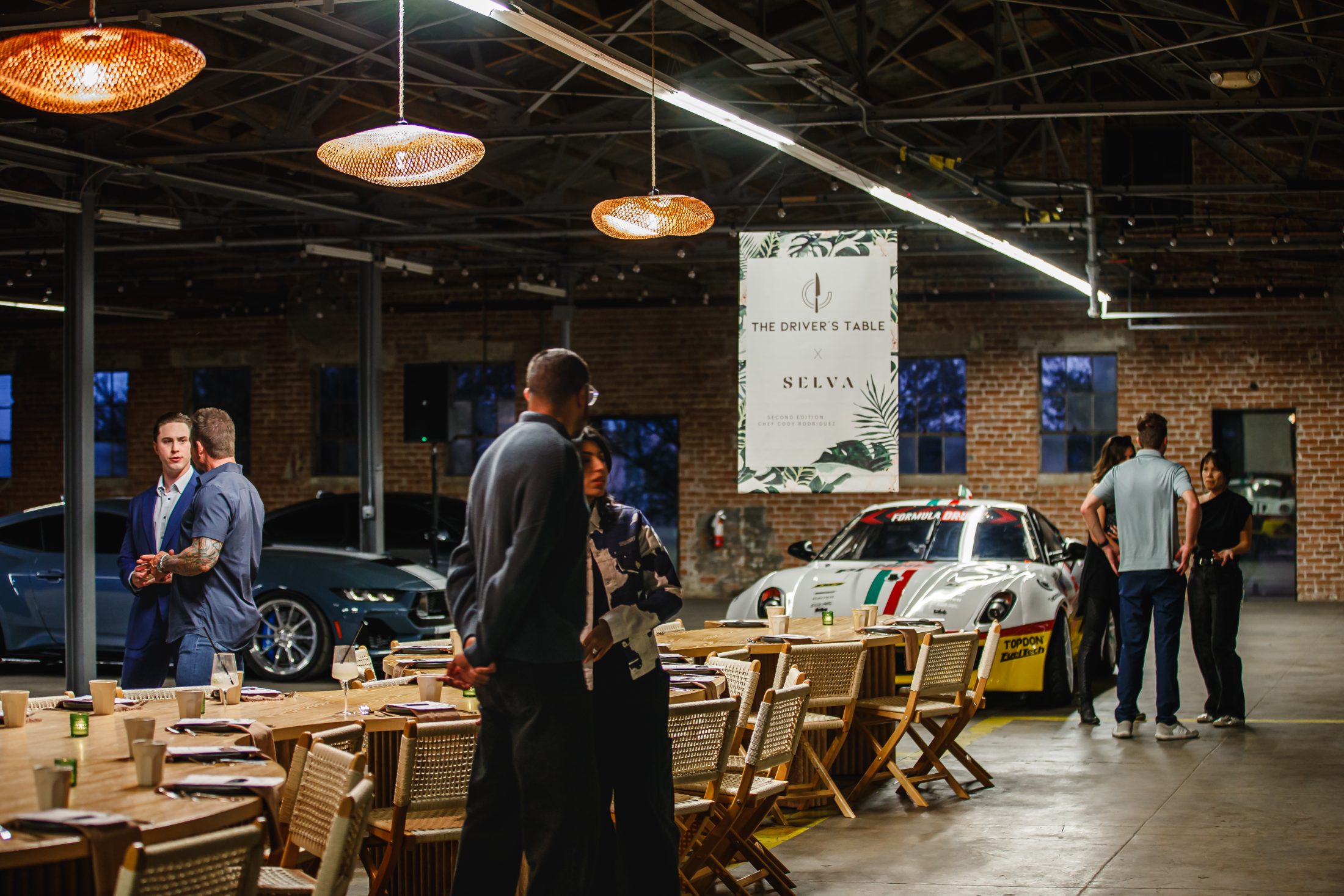 Members gathered at a long table among cars